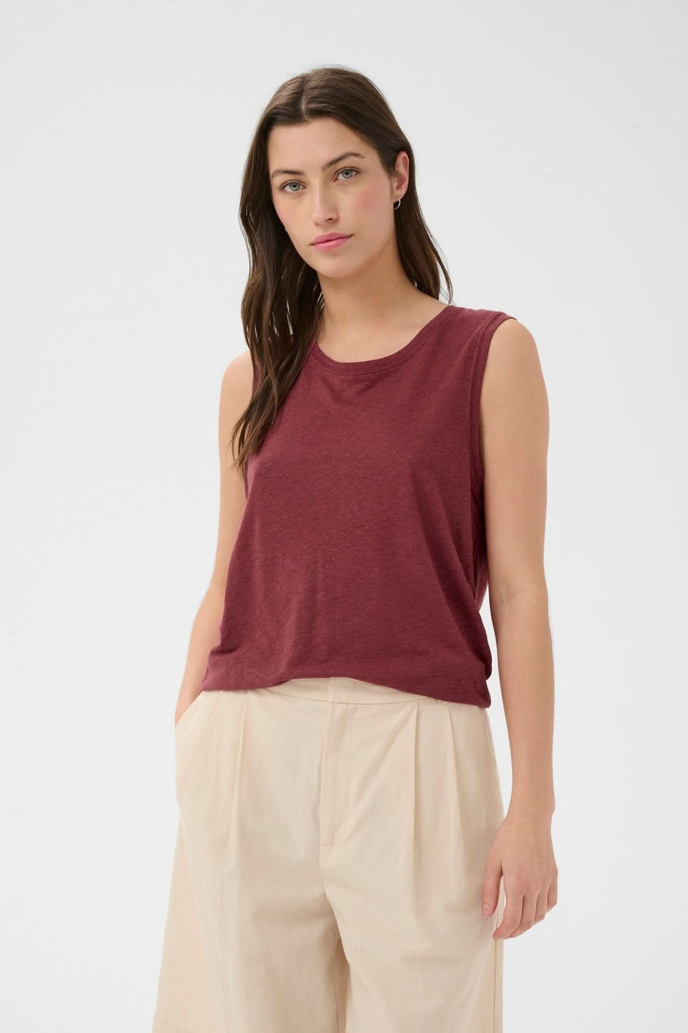 Femme portant la Cami fluide Buena bordeaux sans manches et coupe droite, combinée avec un pantalon beige pour un look polyvalent.