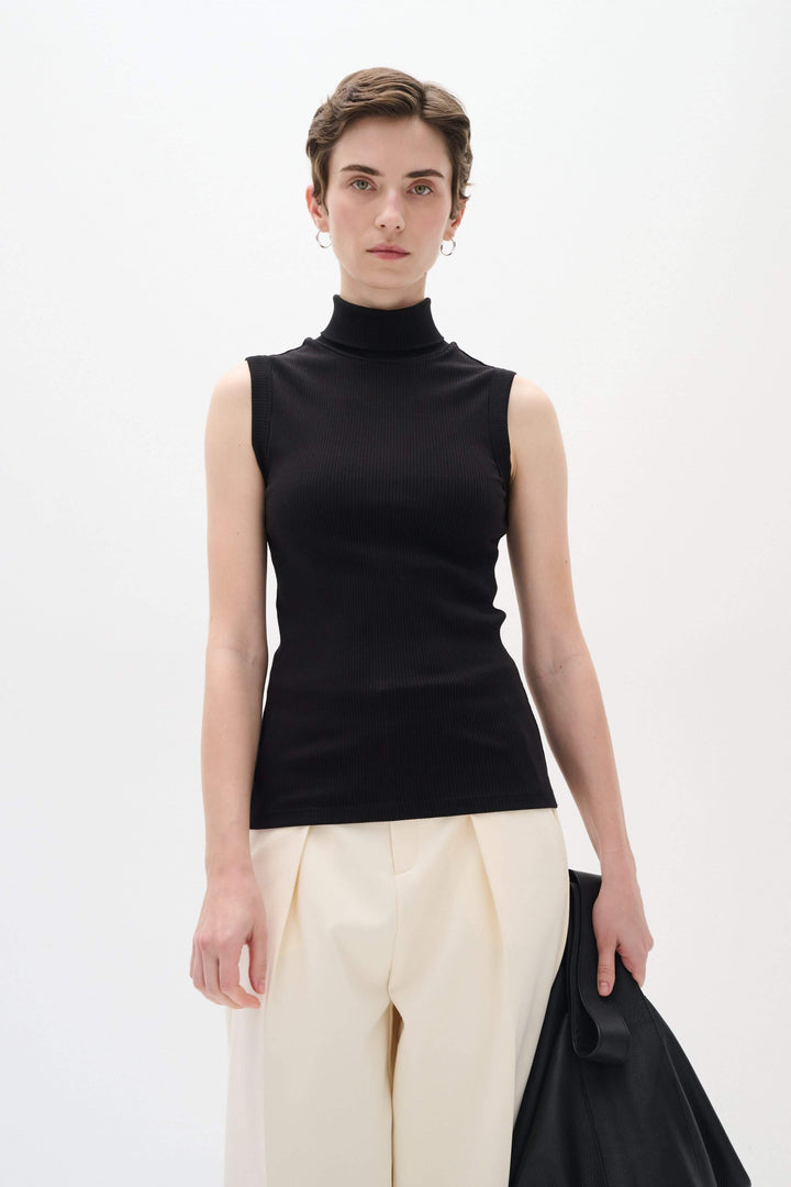 Camisole Dagna en jersey côtelé noir, col montant, sans manches, coupe ajustée, portée avec un pantalon ample.
