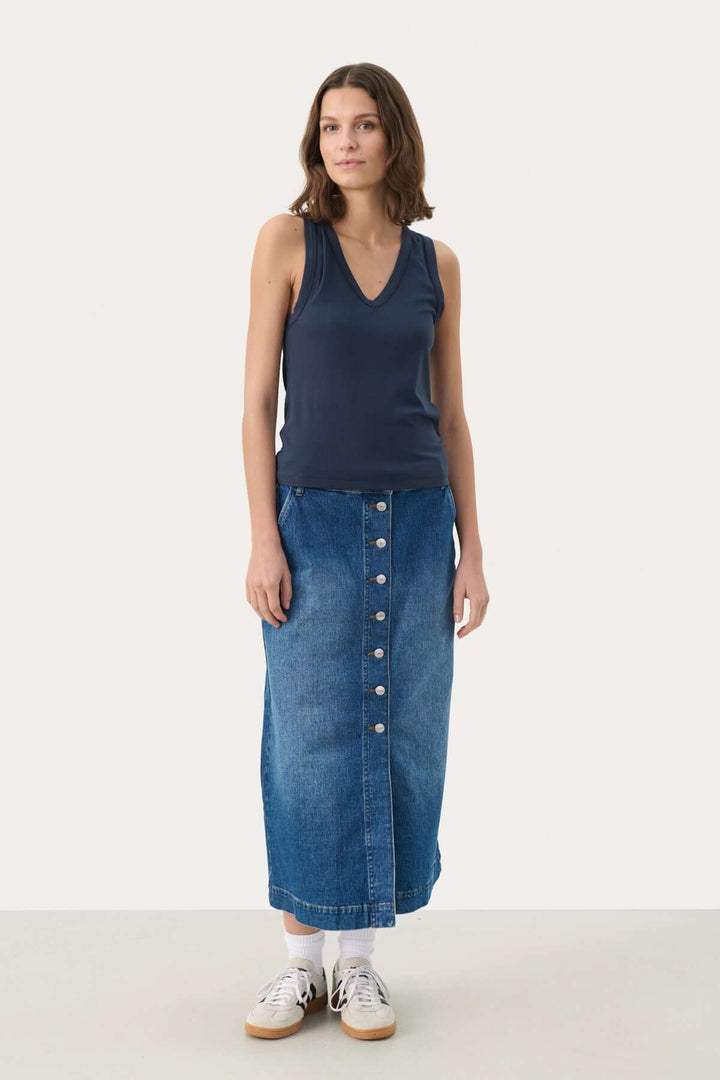 Camisole Nikkia en viscose avec encolure en V, portée avec une jupe en jean et des baskets blanches.