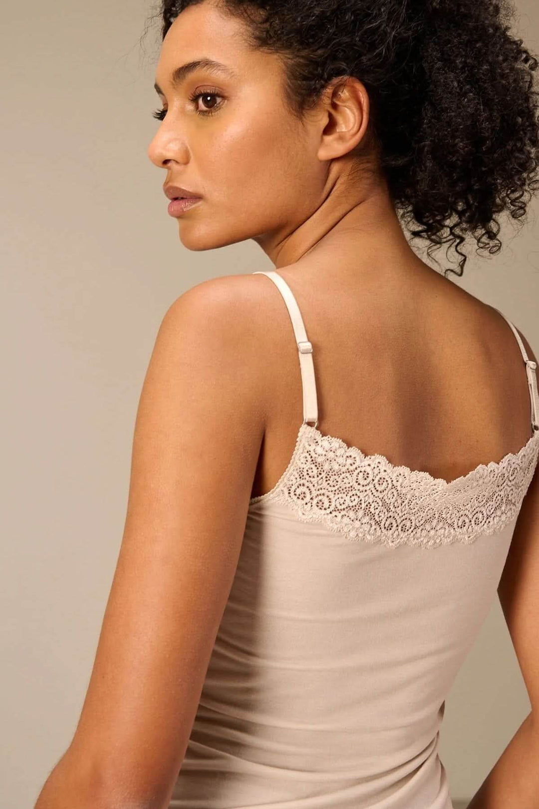 Femme portant une Camisole à bretelles avec dentelle beige vue de dos, mettant en valeur le détail en dentelle fine et la coupe ajustée.