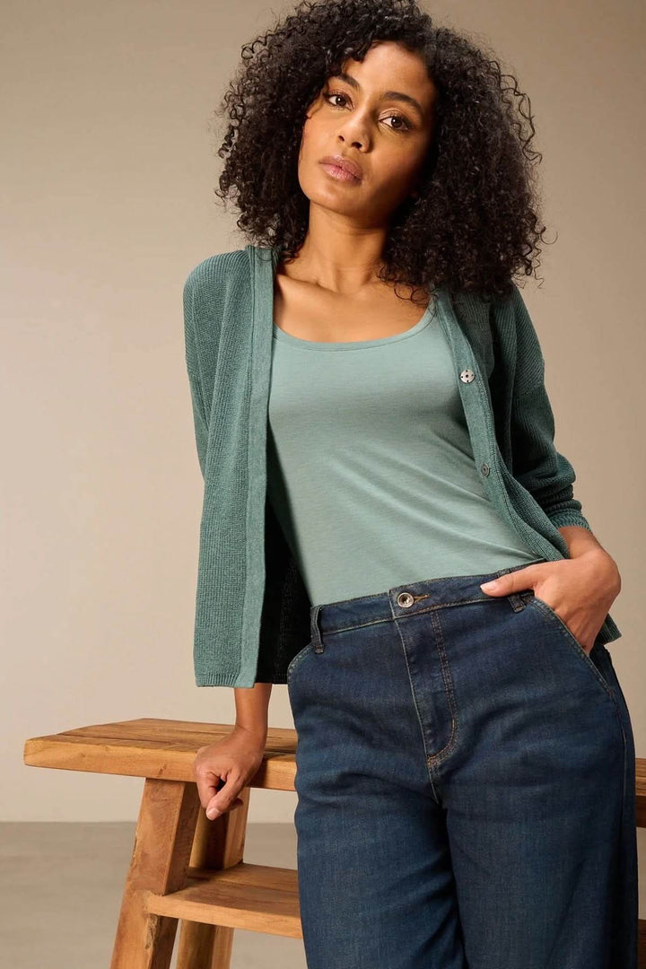 Femme portant une camisole à col rond verte avec un cardigan, posant avec élégance.