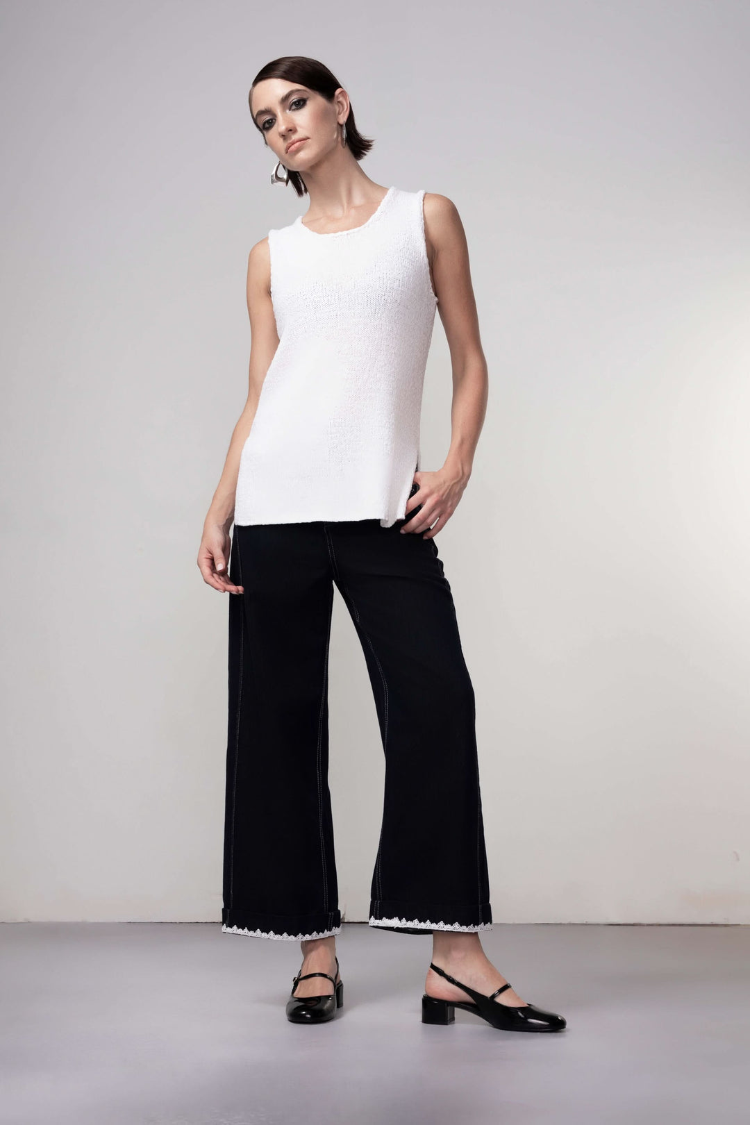 Femme portant une camisole en maille blanche avec pantalon noir pour une tenue minimaliste et élégante.
