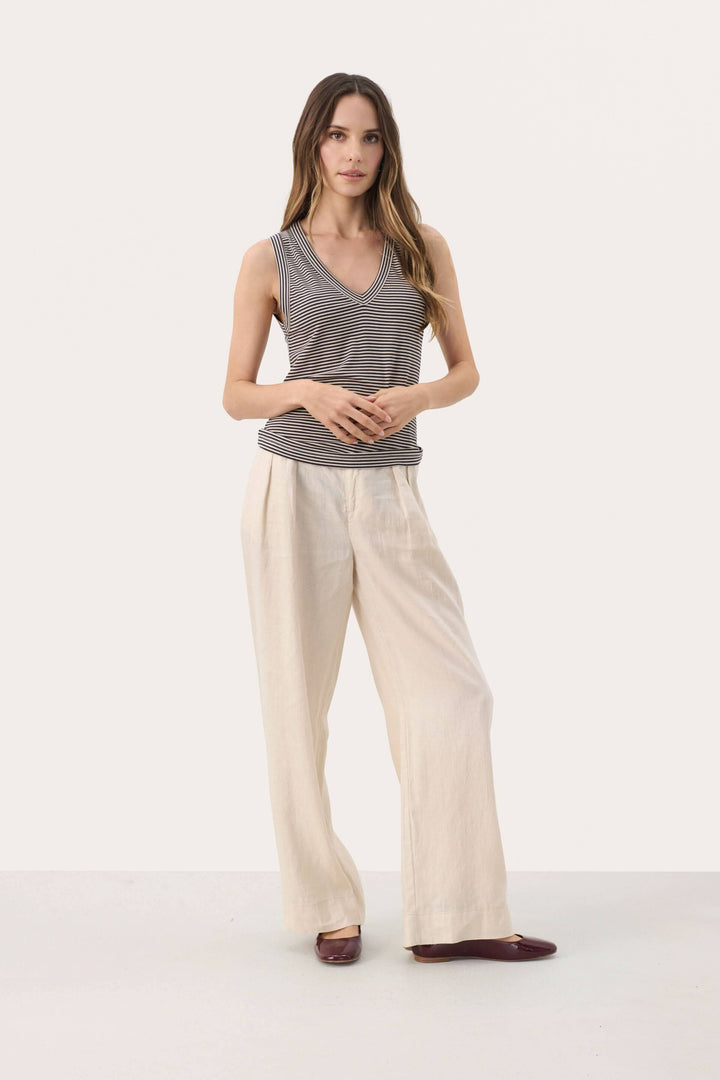 Camisole rayée Nikkia en V, sans manches, portée avec un pantalon large pour un look décontracté et élégant.