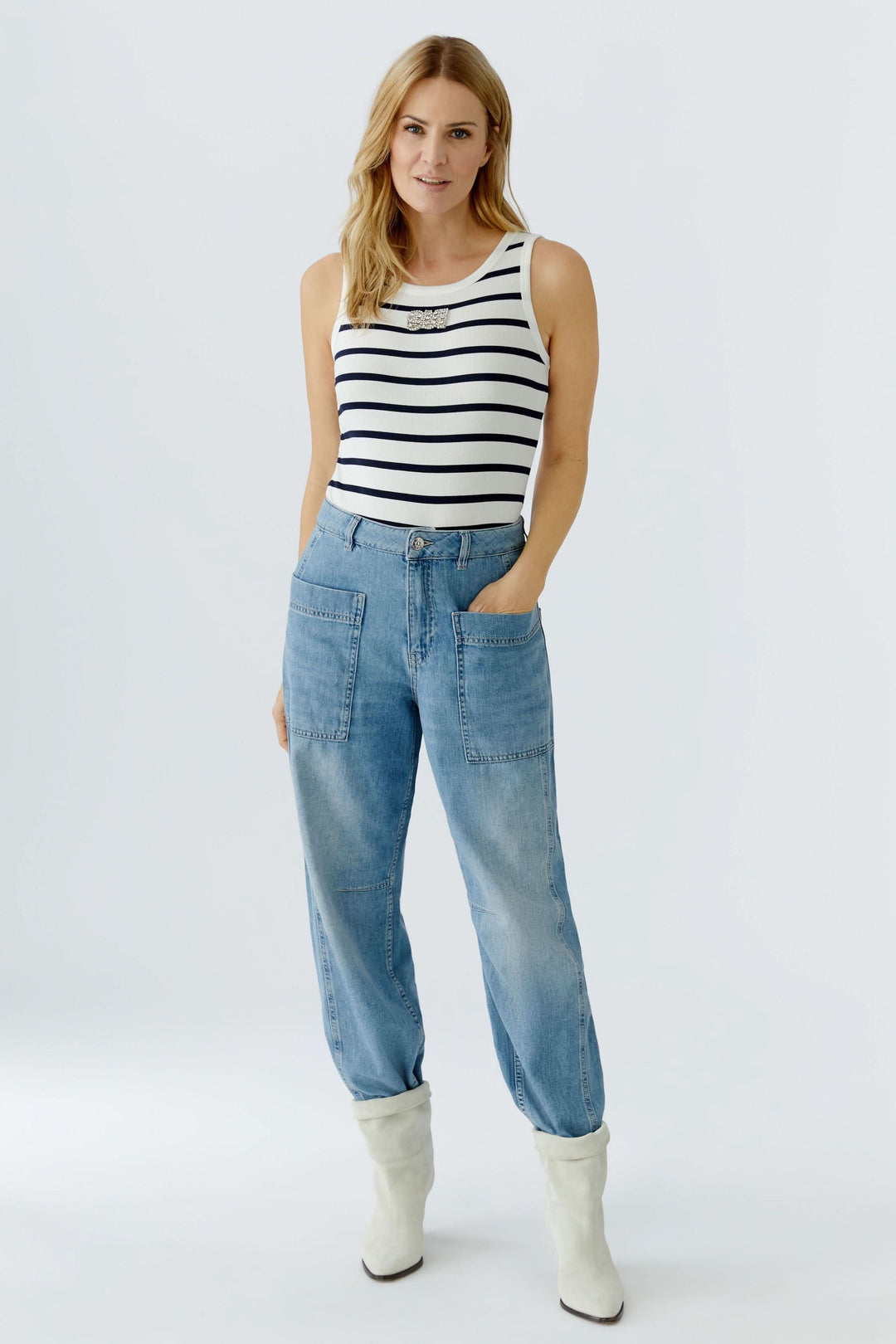 Femme portant une camisole rayée sans manches au motif marin, avec un jean décontracté et des bottes blanches.