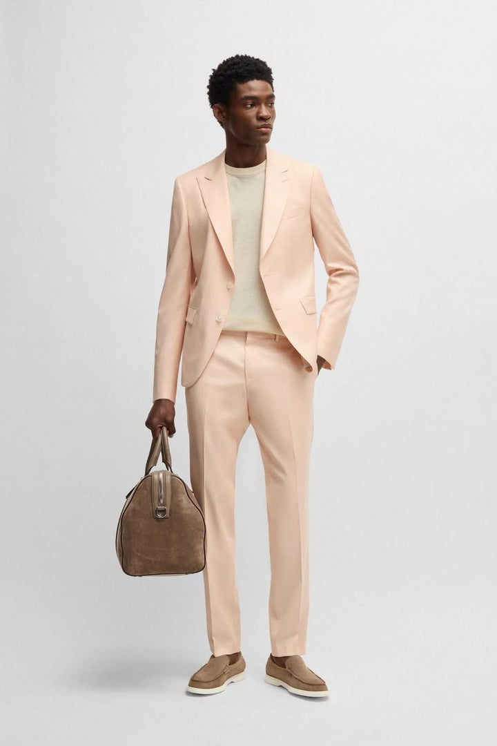 Homme portant un costume rose clair avec un t-shirt beige, tenant un sac à main élégant, look chic et décontracté.