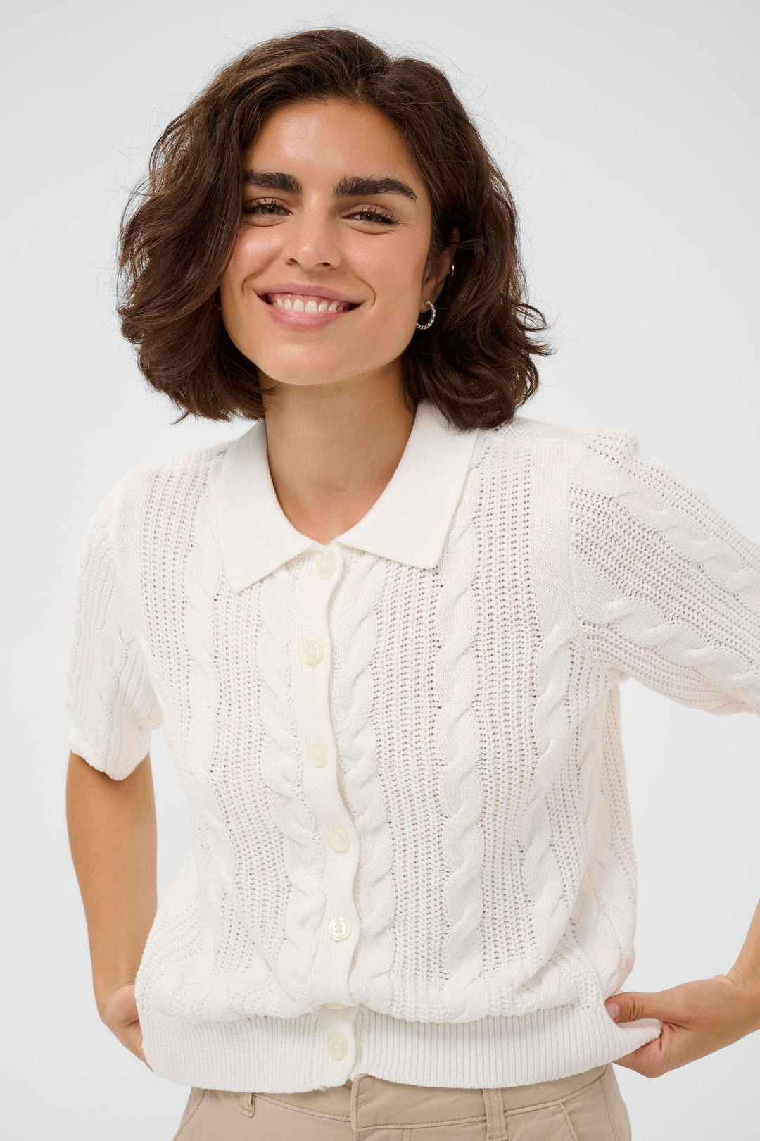 Femme souriante portant le Cardigan Blair blanc en maille torsadée avec col polo et manches courtes. Élégant et confortable.
