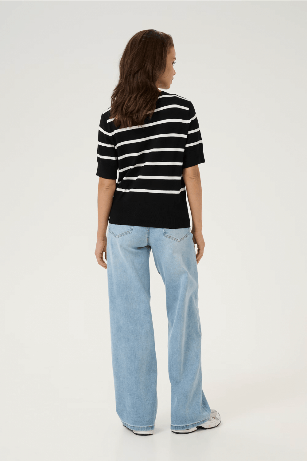 Femme vue de dos portant un cardigan ligné noir et blanc avec un jean en denim bleu clair.