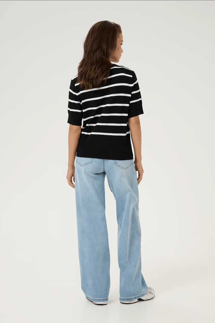 Femme vue de dos portant un cardigan ligné noir et blanc avec un jean en denim bleu clair.