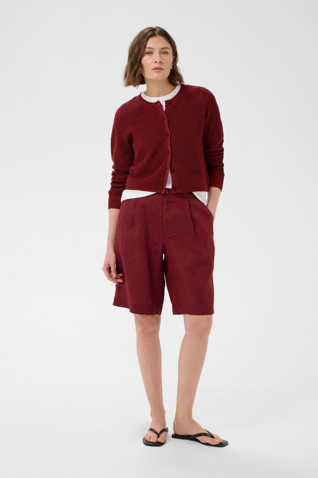 Femme portant le Cardigan boutonné Gigia en maille texturée rouge, manches longues, avec t-shirt blanc et short assorti pour un look décontracté.