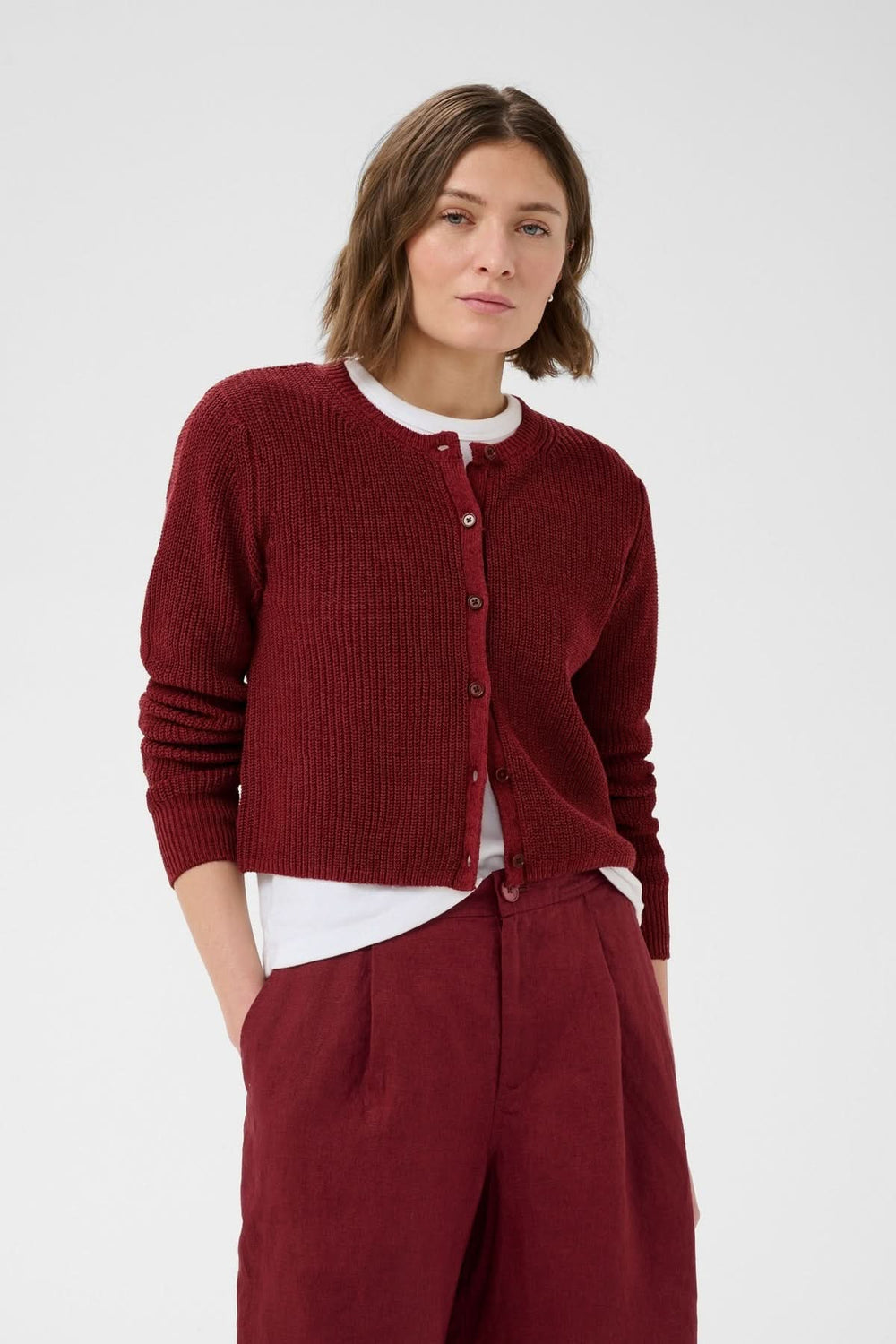 Femme portant un cardigan boutonné Gigia en maille texturée rouge avec une coupe légèrement courte et des manches longues.