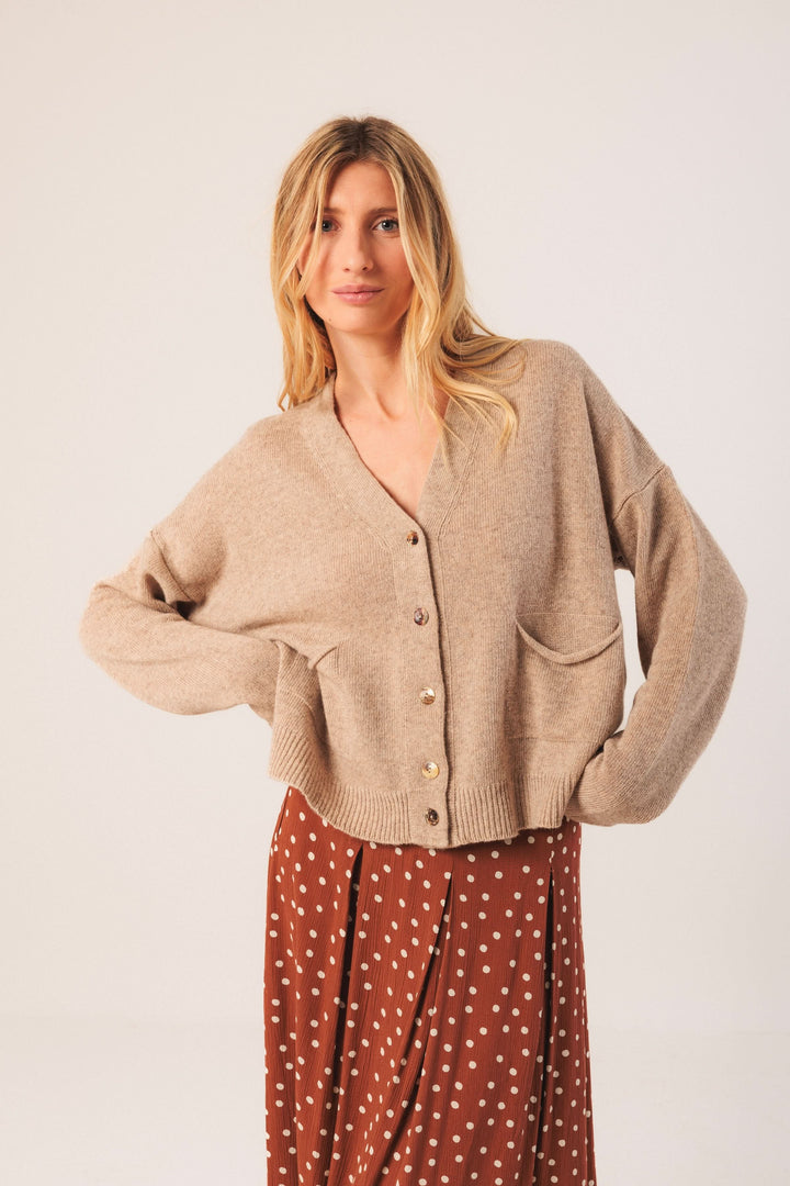 Cardigan court beige à encolure en V, style décontracté, porté avec une jupe à pois, look casual chic.