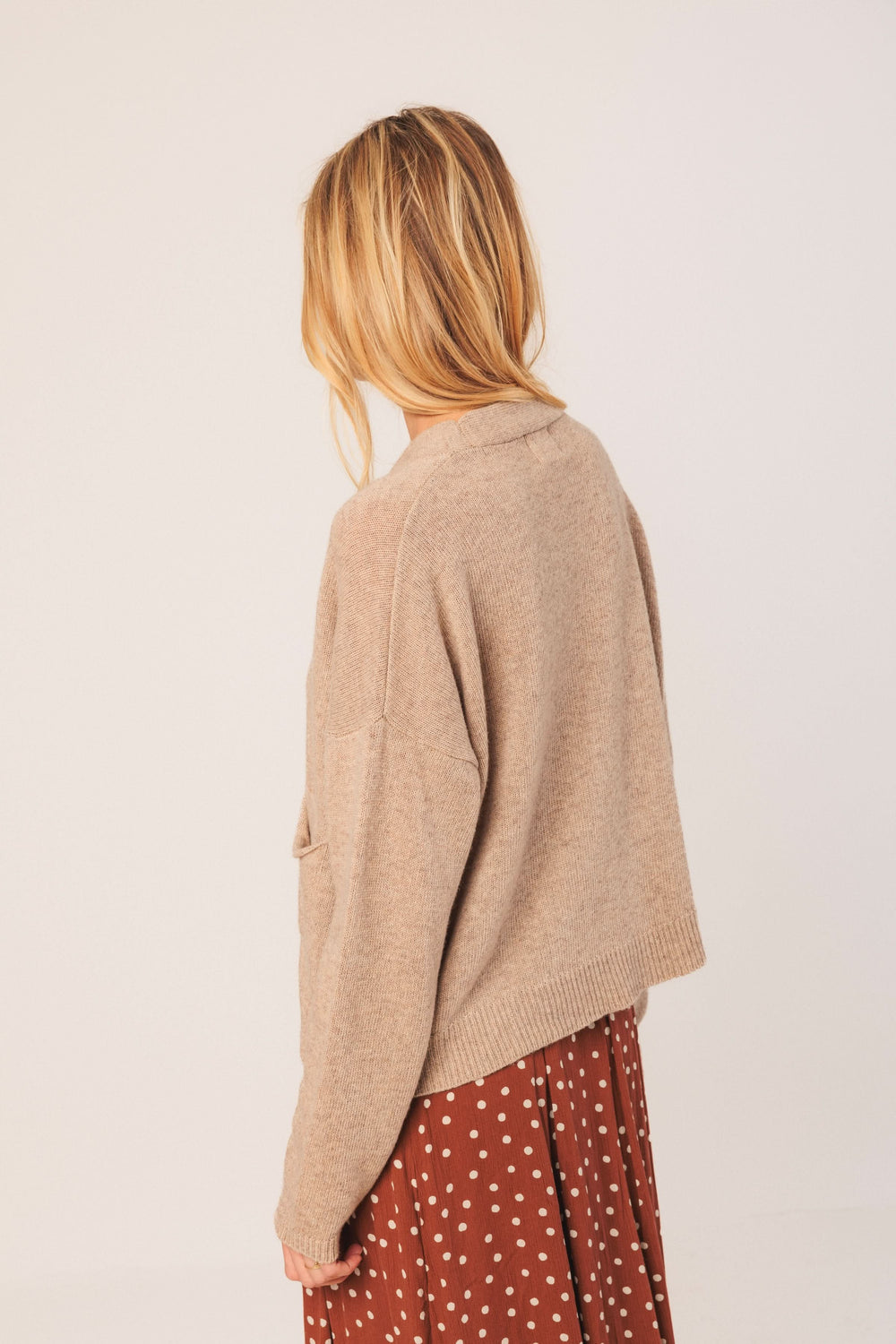 Cardigan court beige avec encolure en V porté sur une jupe à pois, vue arrière.
