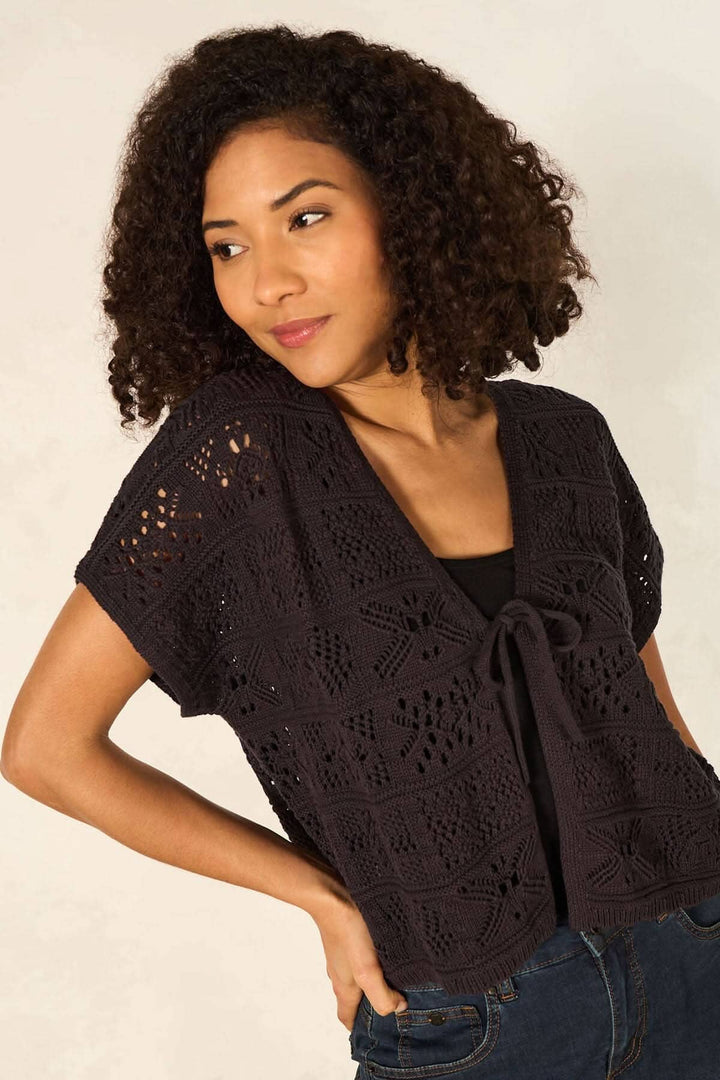 Cardigan en maille ajourée à manches courtes, détail élégant avec ruban, porté par une femme. Idéal pour superposer.