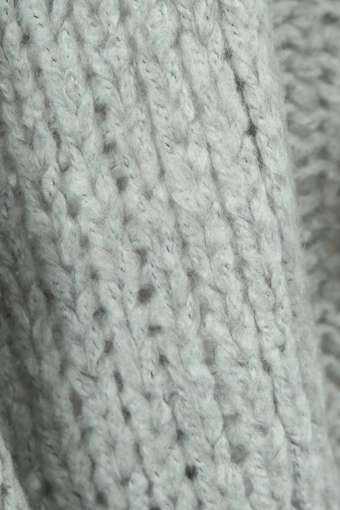 Gros plan sur un tricot en gris, montrant une texture douce et faite main, idéale pour un cardigan sans bouton.