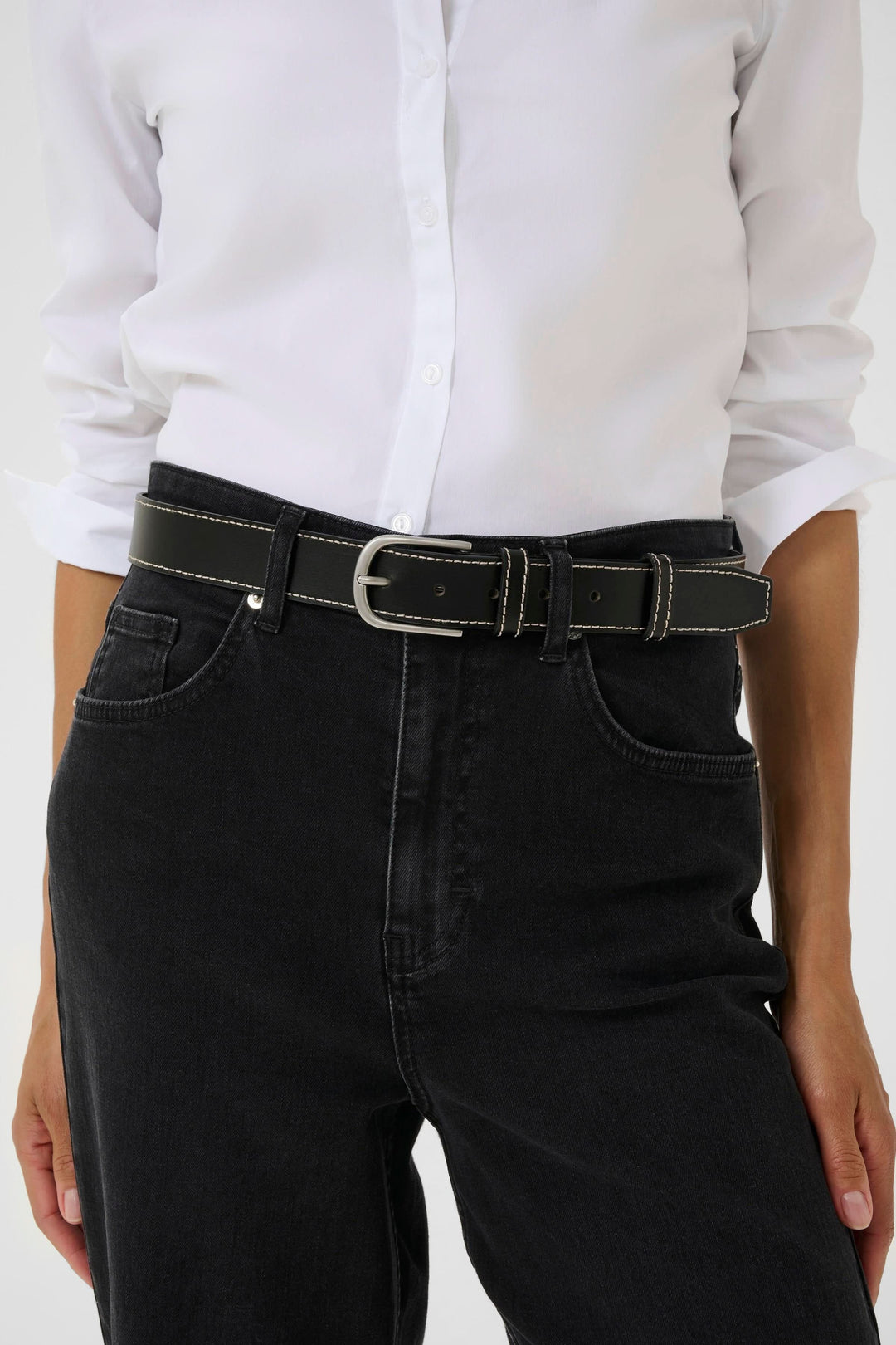 Ceinture Seyra en cuir noir avec surpiqûres contrastantes, portée sur un pantalon noir avec une chemise blanche.