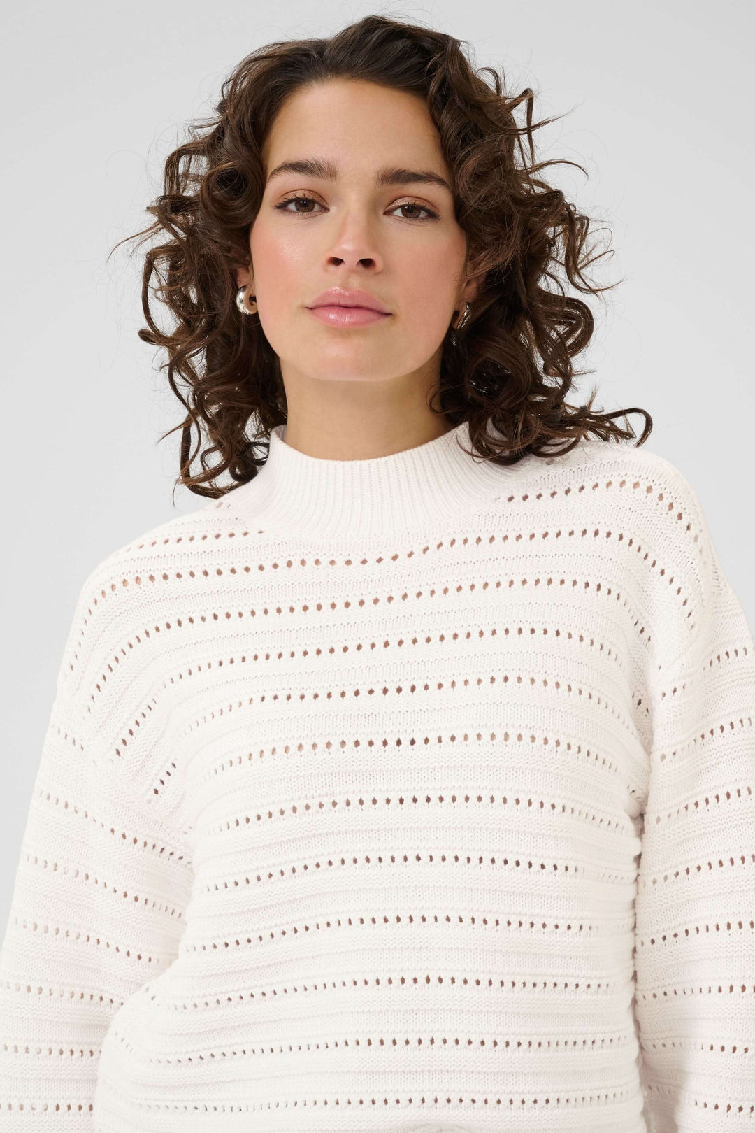 Femme portant le Chandail Dolly en tricot ajouré blanc avec col montant côtelé, manches longues et motif horizontal élégant.