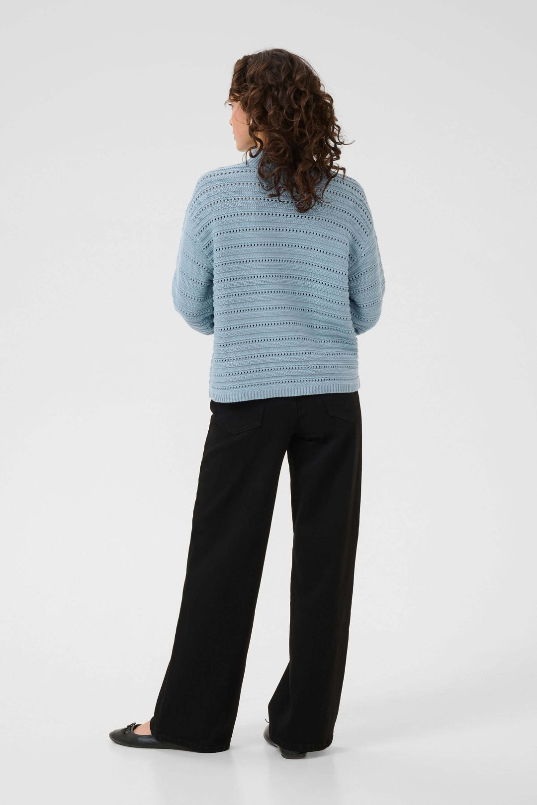 Femme portant le Chandail Dolly en tricot ajouré bleu avec un jean noir, vue de dos, style moderne et raffiné.