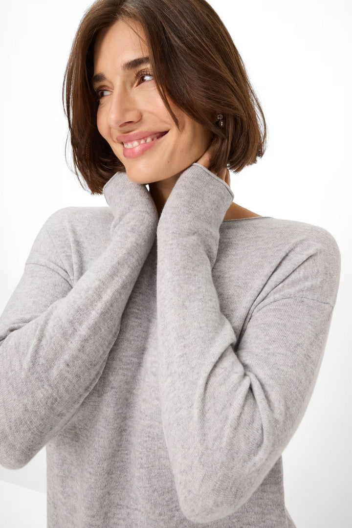 Femme souriant portant un chandail gris en maille fine à col bateau et manches longues.