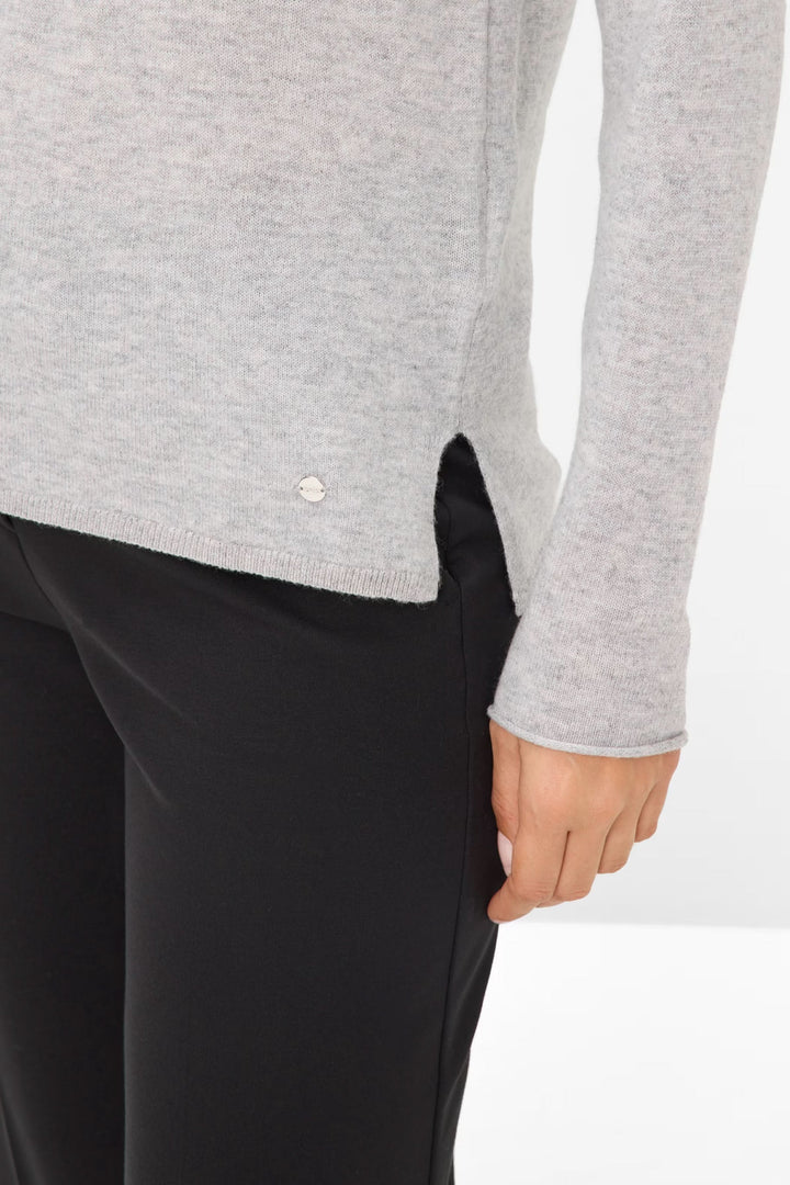 Chandail en maille fine grise avec col bateau, porté avec un pantalon noir, mettant en avant sa coupe droite.