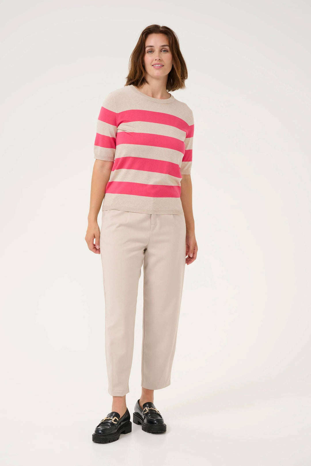 Chandail Lizza à manches courtes, motif ligné rose et beige, porté avec un pantalon beige et des chaussures noires.