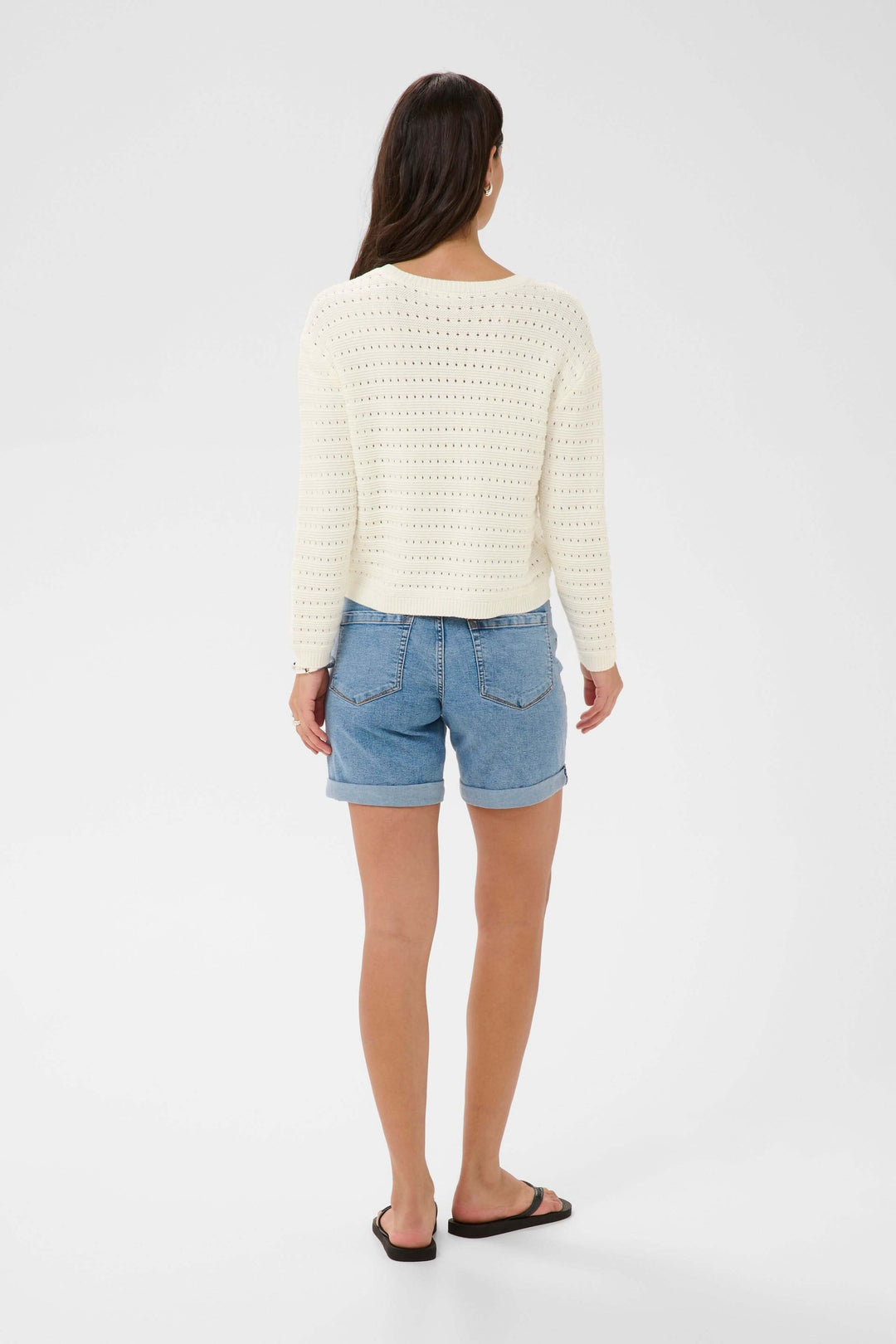 Femme portant le Chandail Metta en maille ajourée blanche, vue de dos, avec short en jean.