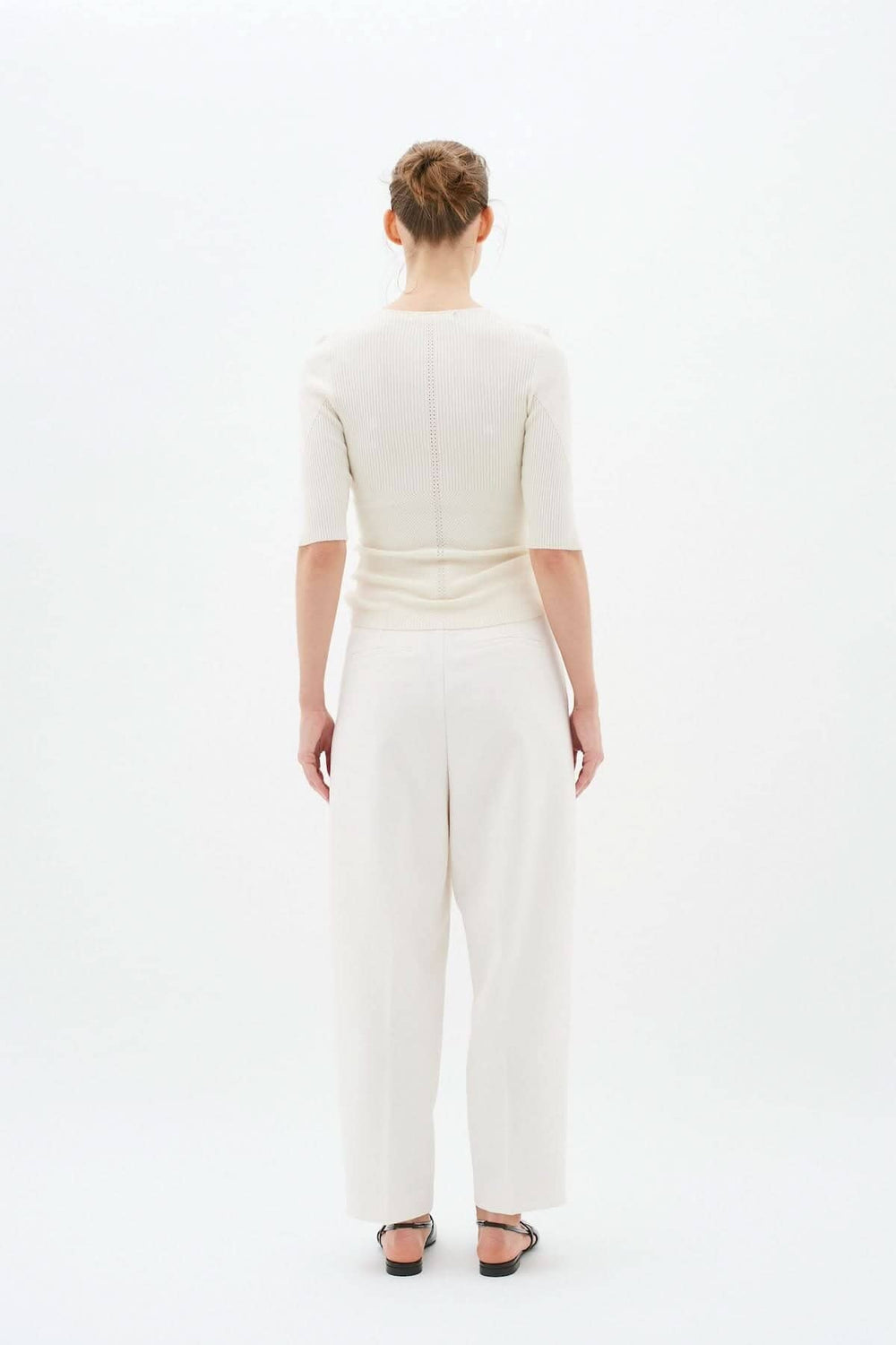 Vue arrière d'une femme portant un chandail ajusté à manches 1/2 avec un pantalon blanc élégant.