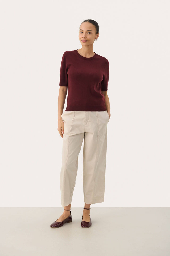 Chandail Natanya en tricot bordeaux à manches courtes, porté avec un pantalon clair pour un look élégant.