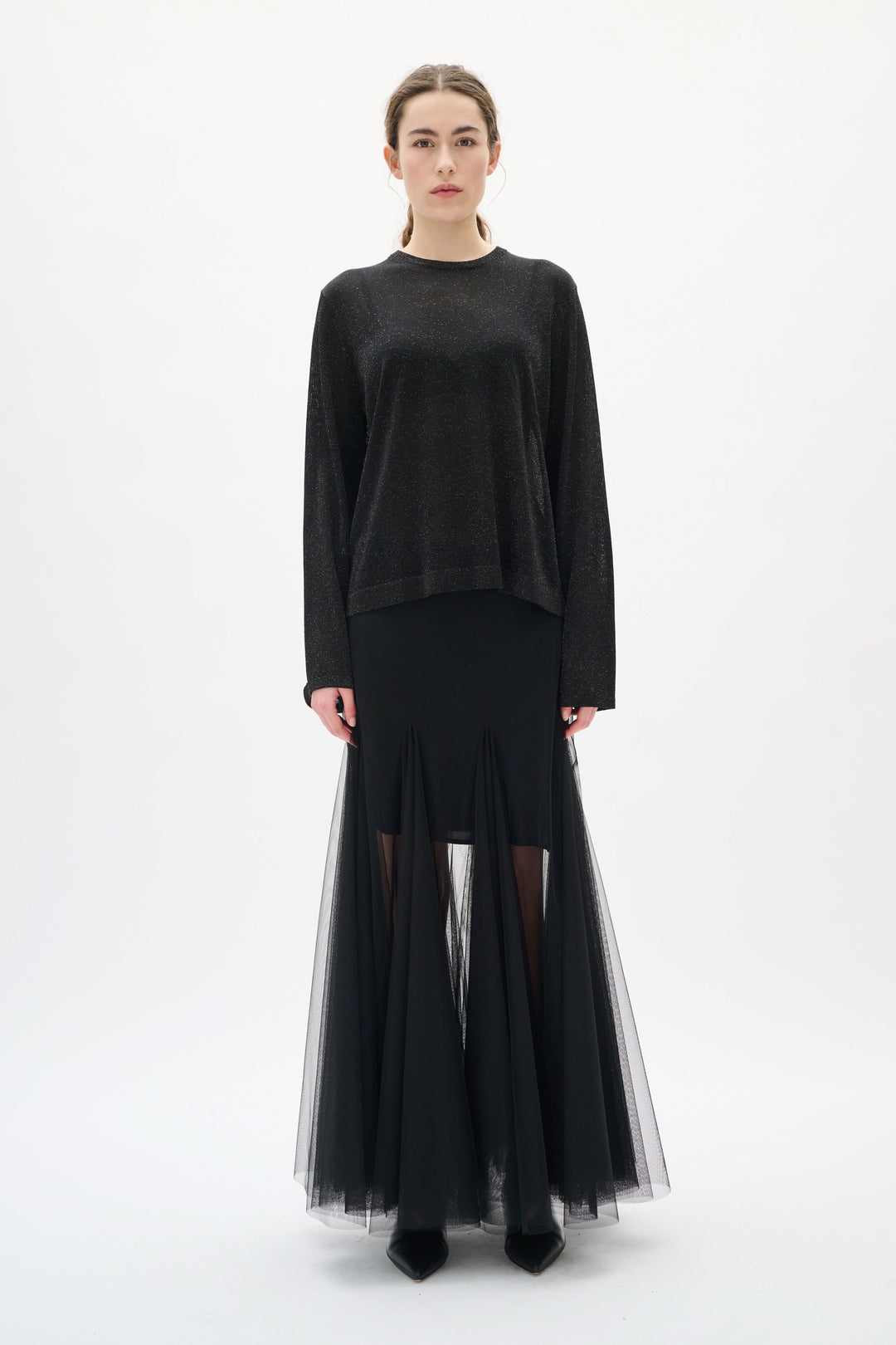 Femme portant un chandail Thani à effet scintillant noir avec jupe transparente, manches longues et coupe fluide pour une tenue élégante.