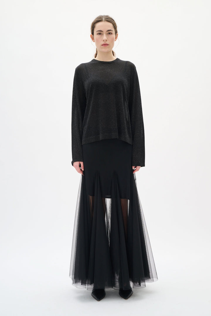 Femme portant un chandail Thani à effet scintillant noir avec jupe transparente, manches longues et coupe fluide pour une tenue élégante.