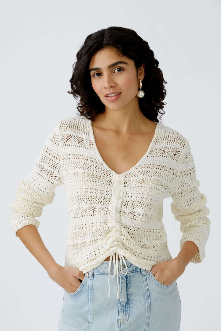Chandail ajouré crème avec décolleté en V et laçage, style décontracté et élégant, porté par une femme.