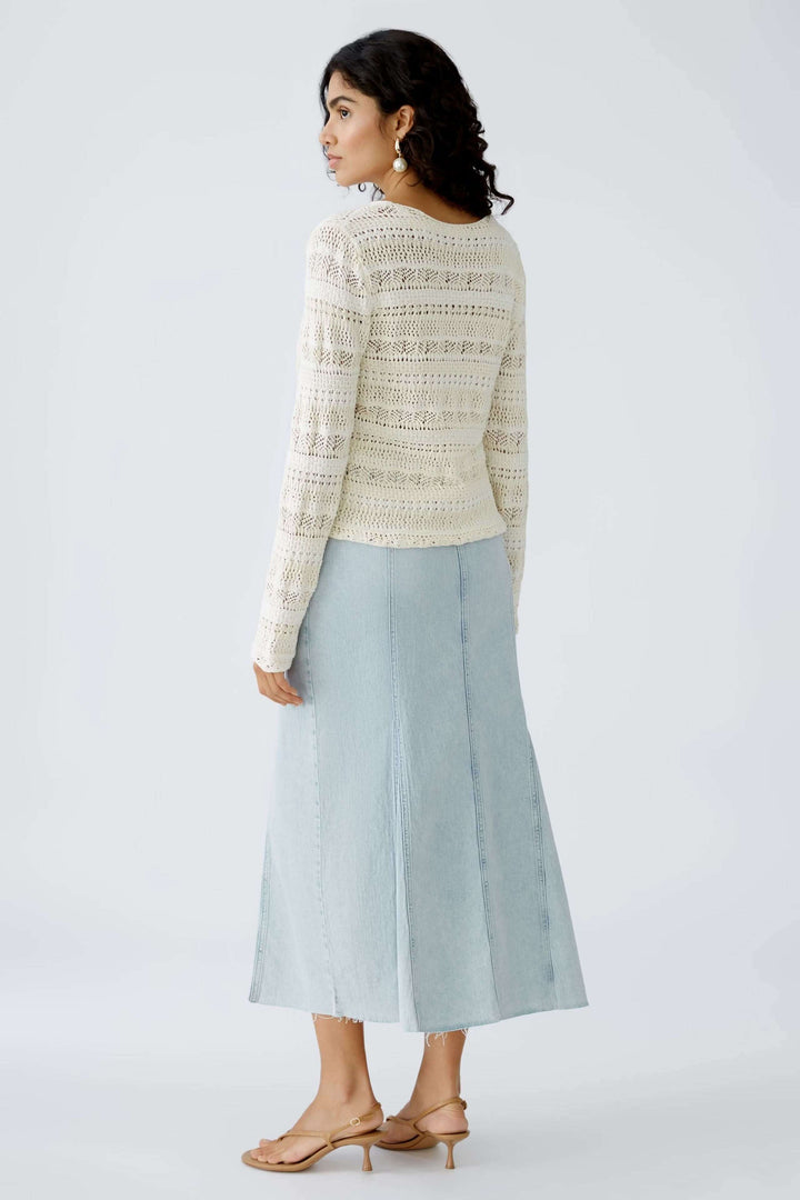 Femme portant un chandail ajouré élégant avec une jupe moderne en denim, vue de dos.