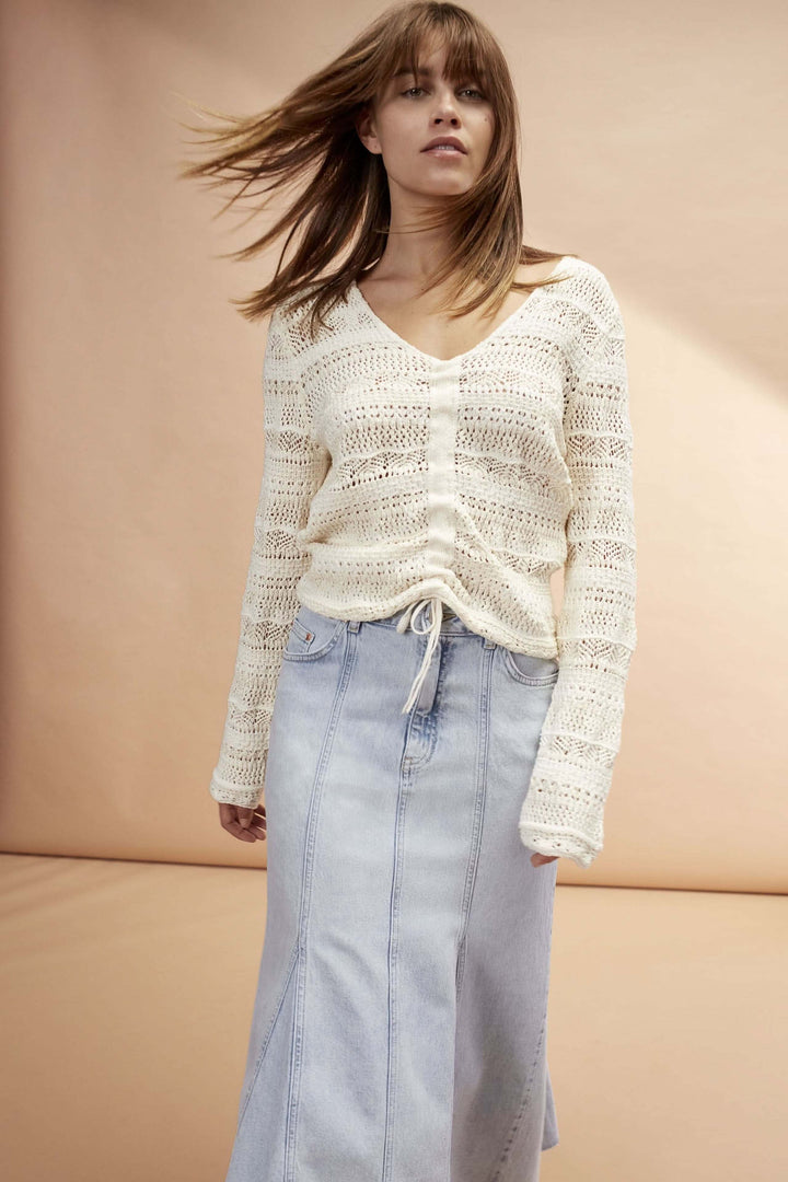 Chandail ajouré élégant avec laçage, décolleté en V, porté avec une jupe en denim.