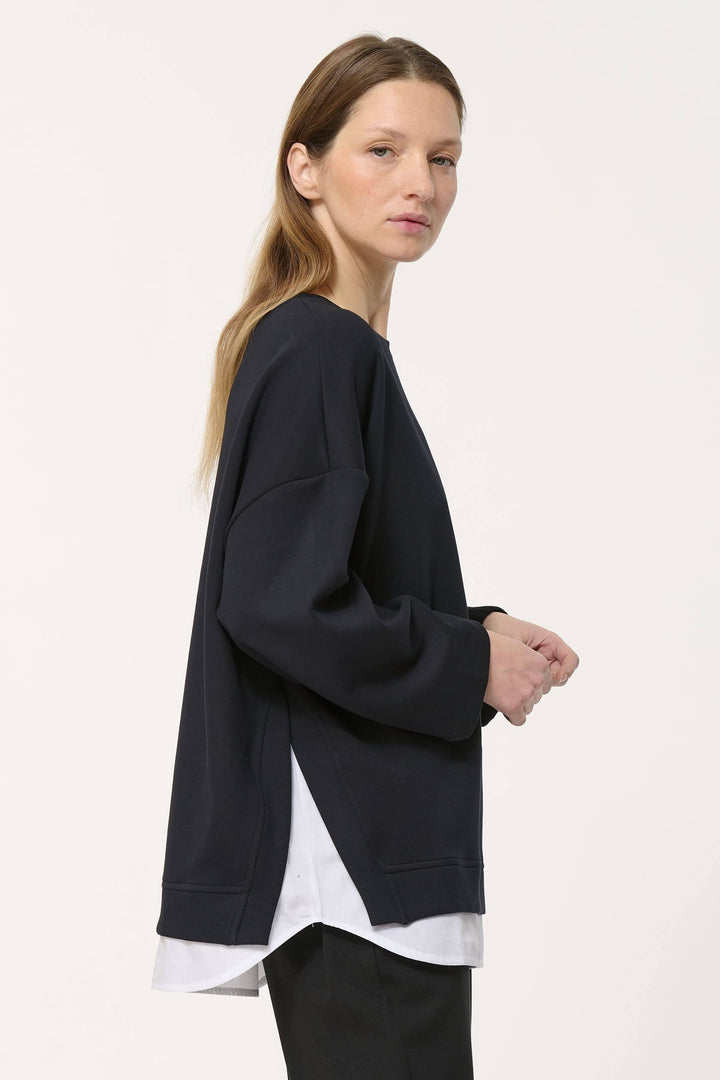 Chandail ample noir au style minimaliste avec superposition blanche, coupe oversize et décontractée.