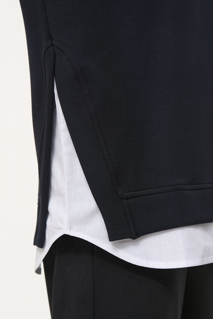 Chamail ample noir avec superposition de chemise blanche, détails oversize et ourlet arrondi.