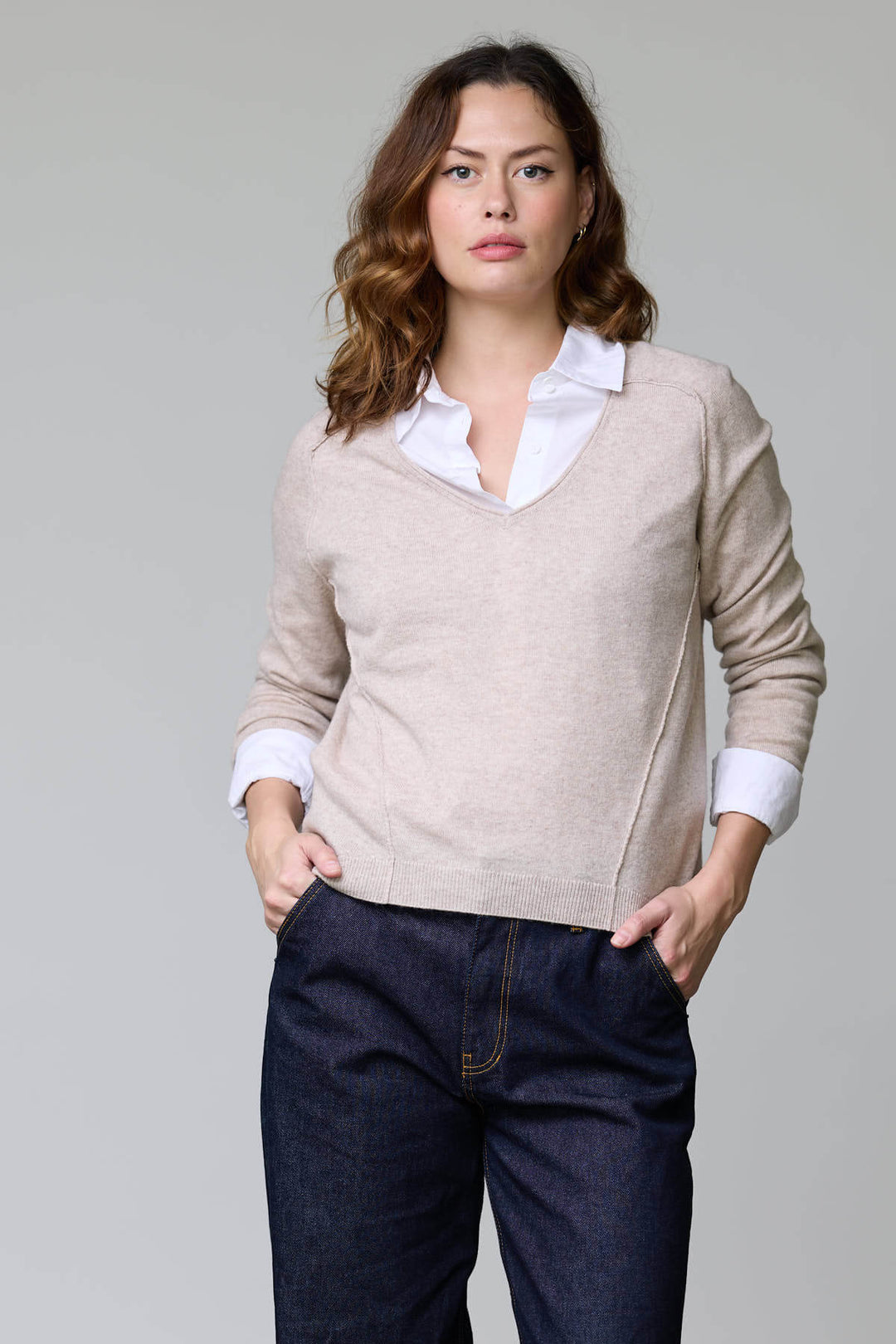 Femme portant un chandail col en V classique beige avec chemise blanche et jeans, style élégant et polyvalent.