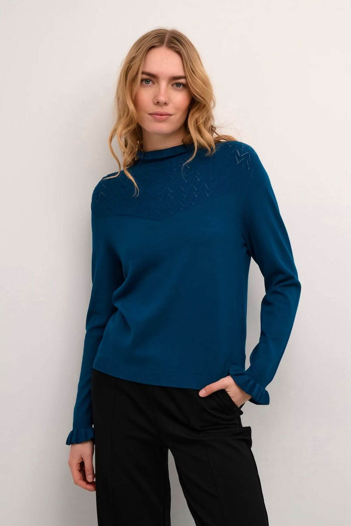 Femme portant un chandail à col montant bleu avec détails ajourés, coupe fluide et élégante.