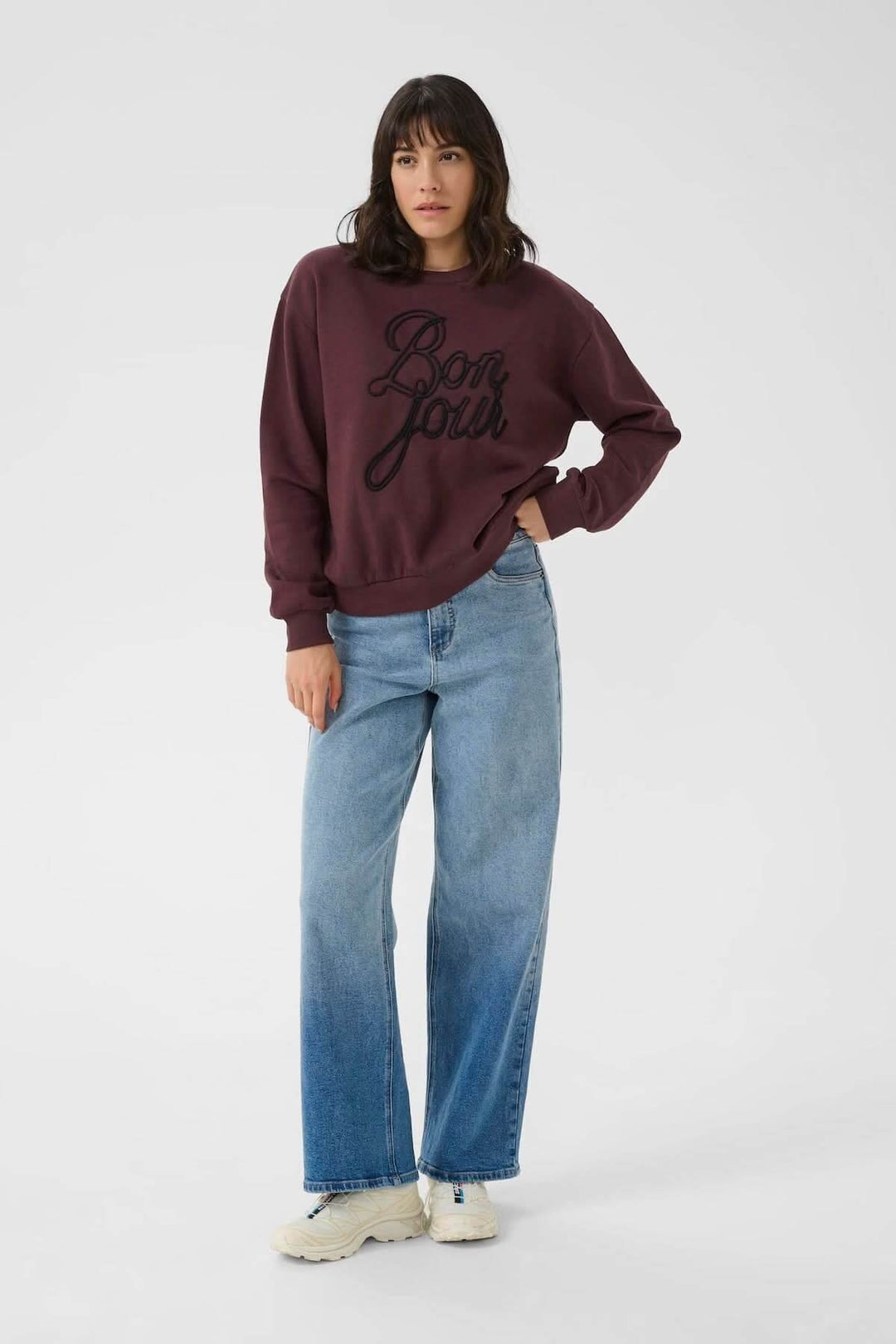 Chandail à col rond bordeaux avec inscription brodée 'Bonjour', associé à un look décontracté et moderne.