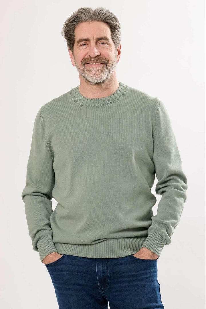 Homme souriant portant un chandail à col rond vert près du corps, parfait pour un look décontracté et élégant.