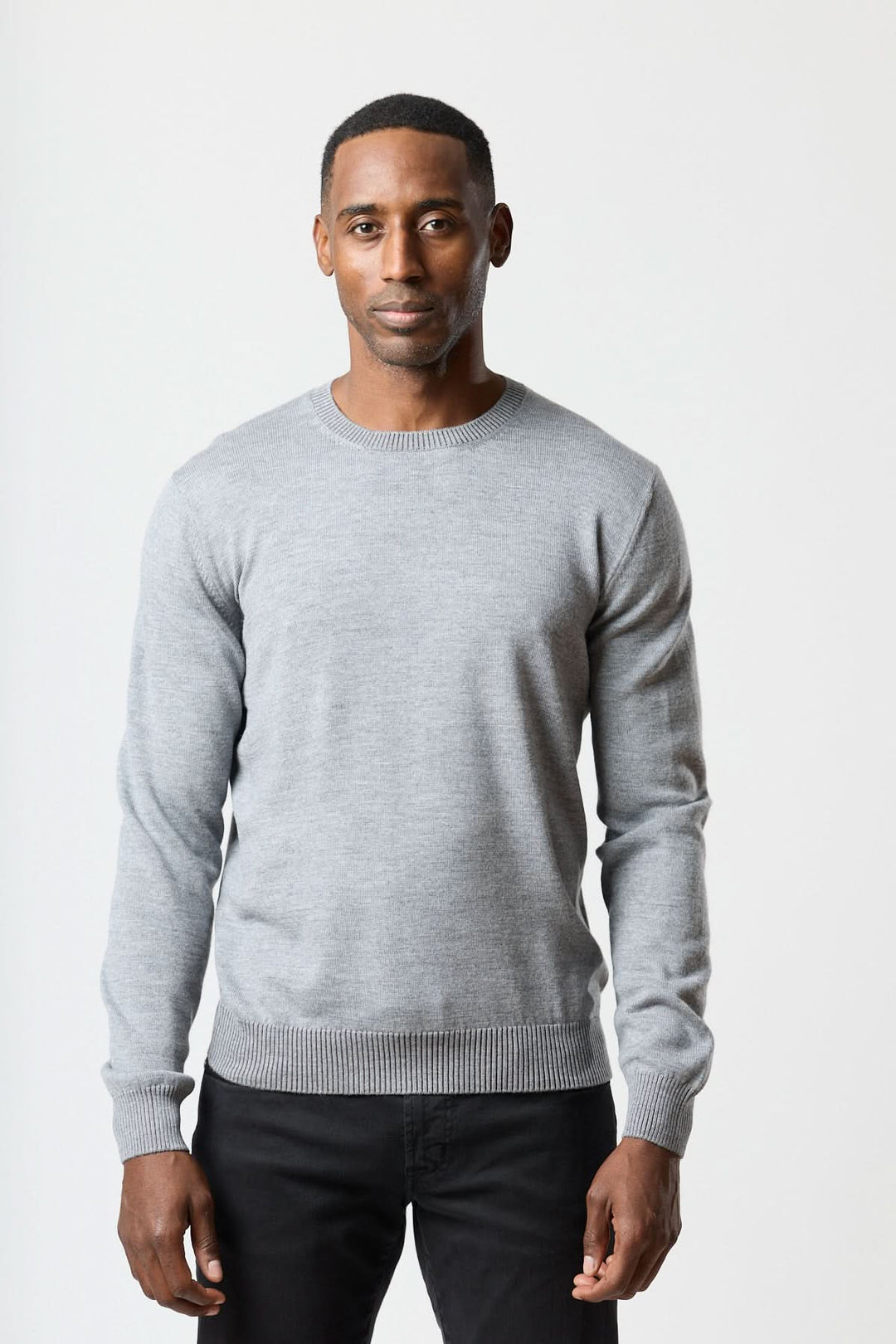 Homme portant un Chandail col rond essentiel gris avec finitions côtelées, style moderne et confortable.