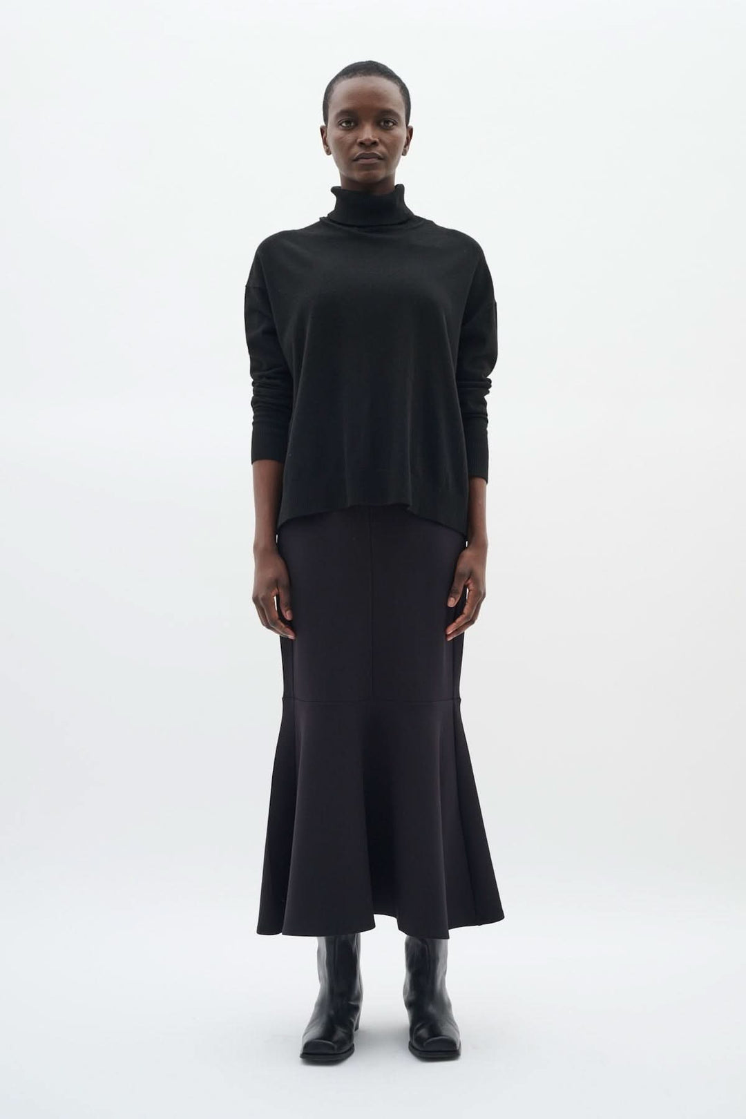Chandail à col roulé coupe décontractée Glea noir avec manches longues et finitions côtelées, porté avec une jupe pour un look chic.