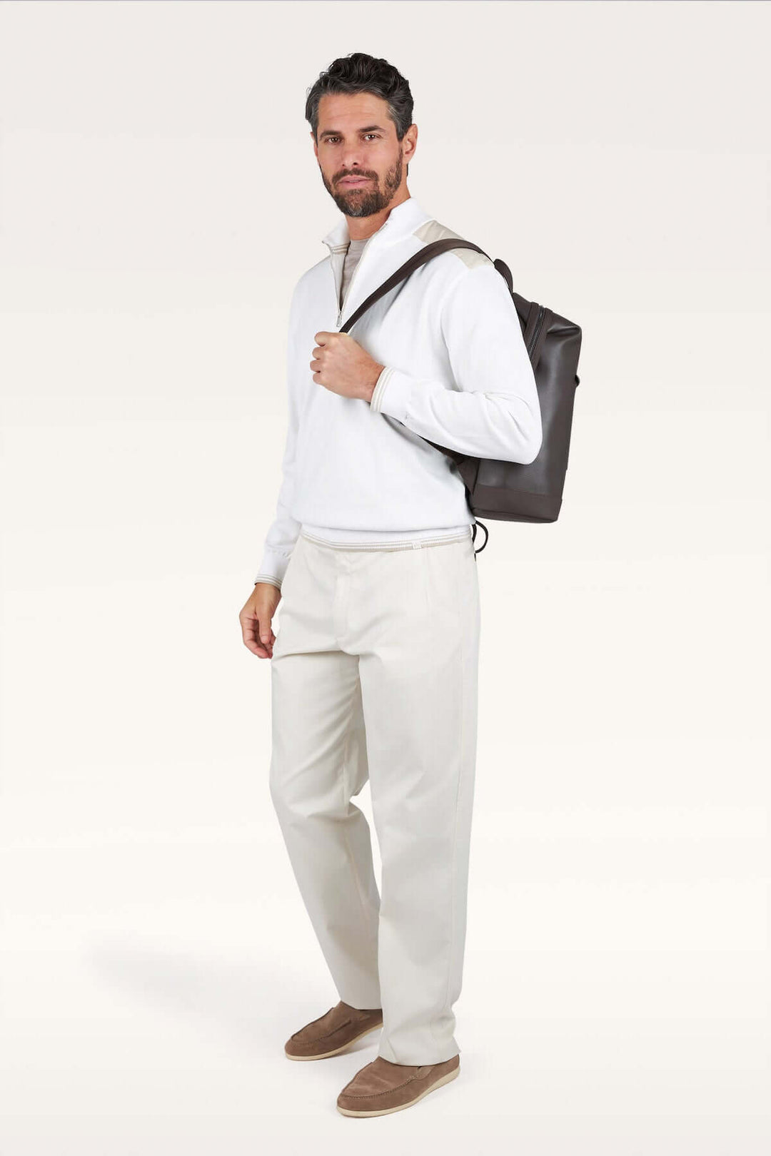 Homme portant un chandail à demi-zip blanc et un sac à dos noir, style décontracté chic.