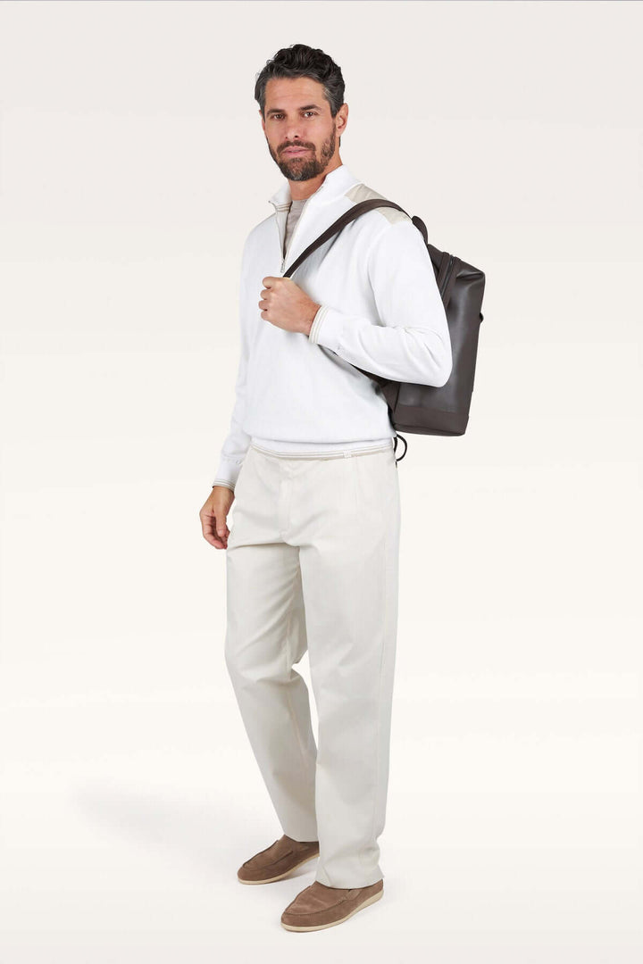 Homme portant un chandail à demi-zip blanc et un sac à dos noir, style décontracté chic.
