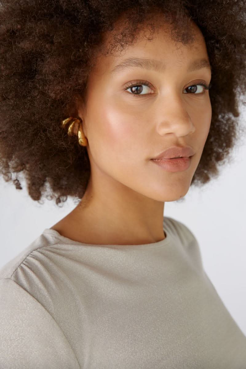 Femme avec cheveux crépus, portant un chandail brillant et des boucles d&