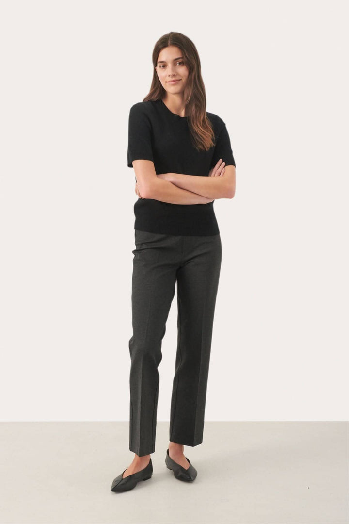 Femme portant un chandail en cachemire noir à manches courtes et un pantalon gris, style élégant et moderne.