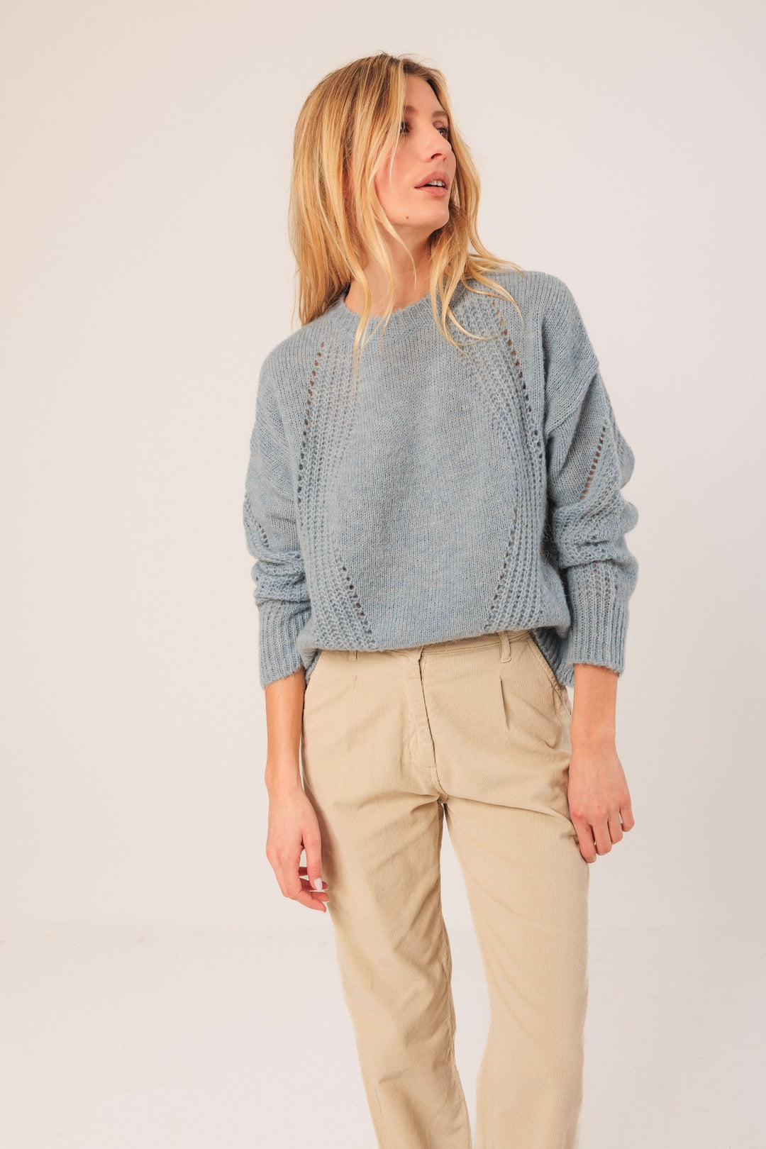 Chandail en maille légère bleu clair avec détails ajourés, porté avec un pantalon beige, style décontracté.