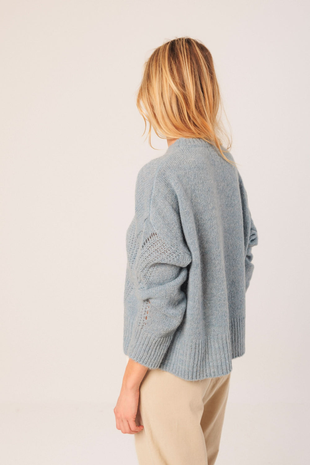Chandail en maille légère bleu, coupe droite avec détails ajourés, porté avec un style décontracté.