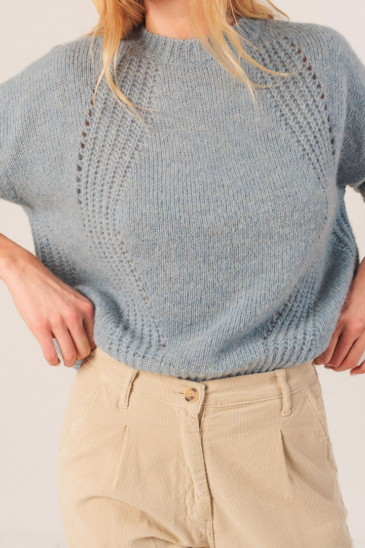 Chandail en maille légère bleu avec détails ajourés, col rond et coupe décontractée, porté avec un pantalon beige.
