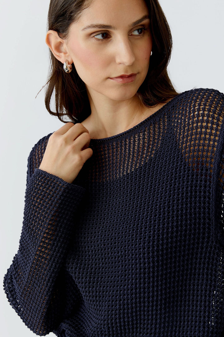 Femme portant un chandail en maille ajourée à manches longues, style moderne et transparent, idéal pour superposer sur une camisole.