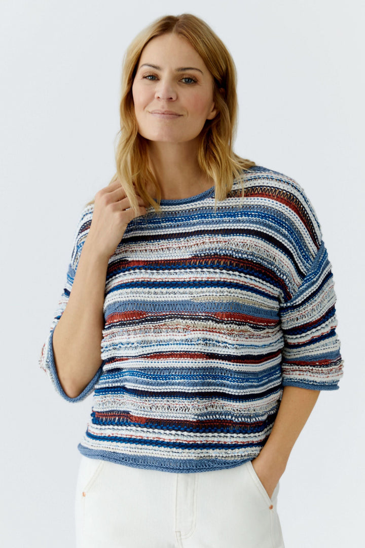 Femme portant un chandail en maille multicolore à manches trois-quarts avec motif rayé, idéale pour un look décontracté-chic.