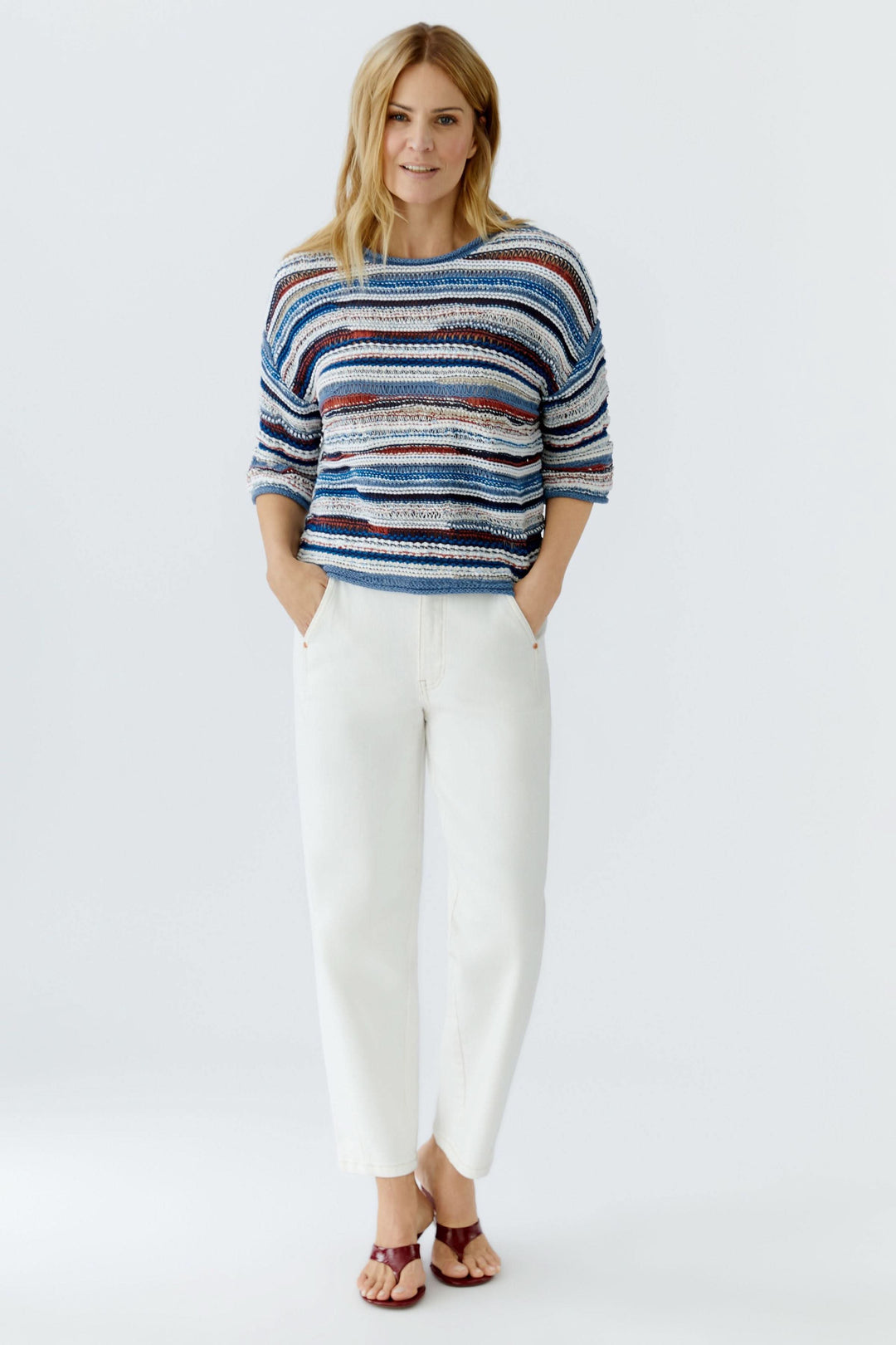 Femme portant un chandail en maille multicolore à manches trois-quarts avec un motif rayé, associé à un pantalon blanc pour un look décontracté.